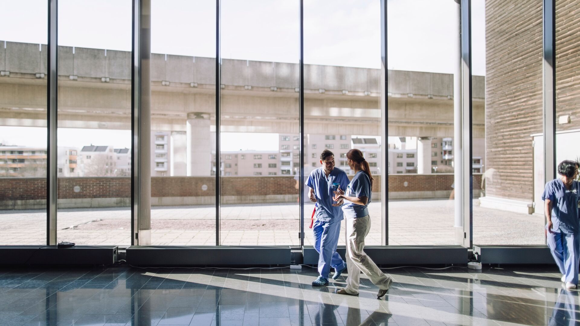 A male and female medical workers walking near glass windows at a hospital