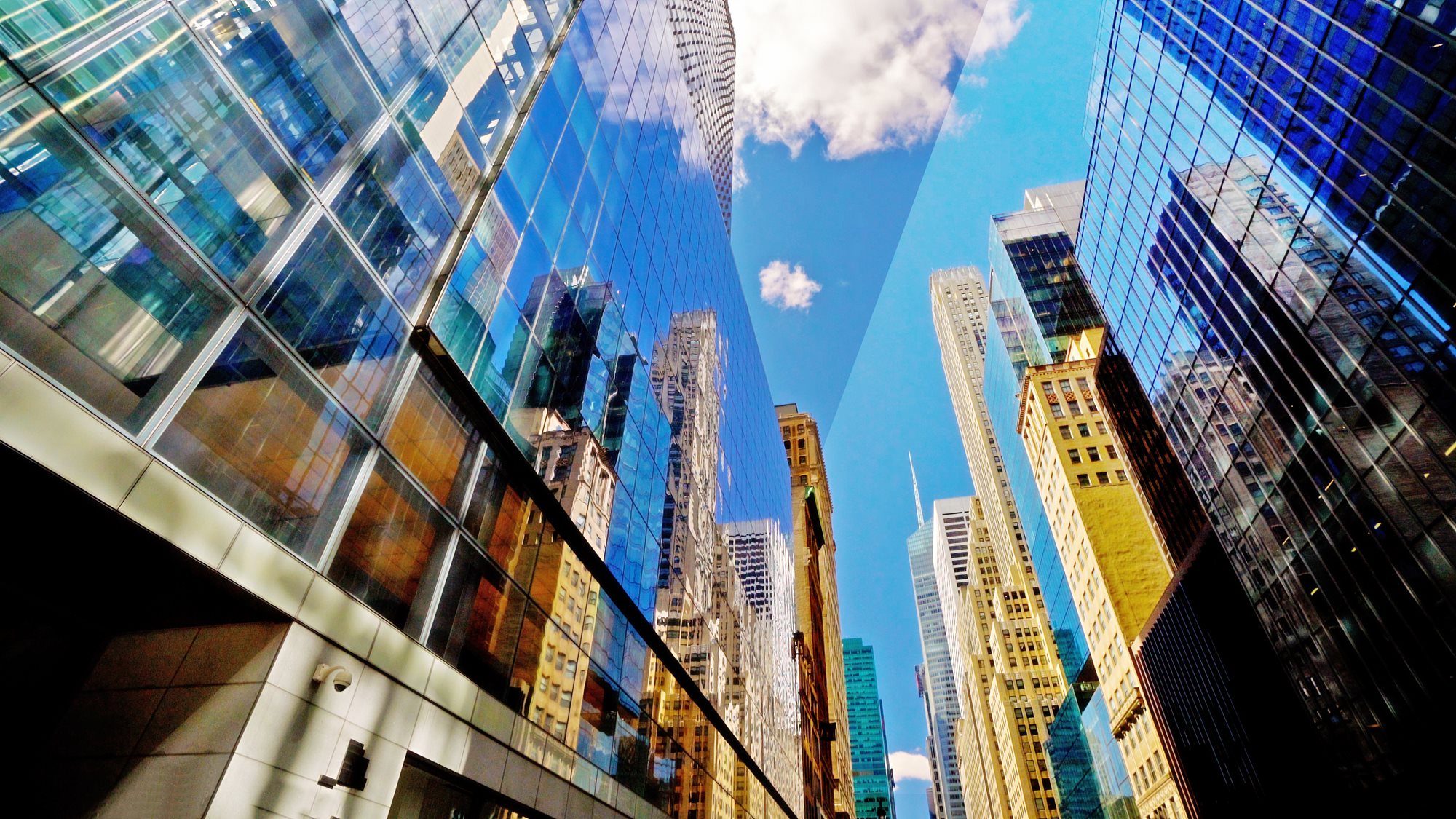 Low‑angle view of tall glass skyscrapers reflecting neighboring buildings and a blue sky with scattered clouds.