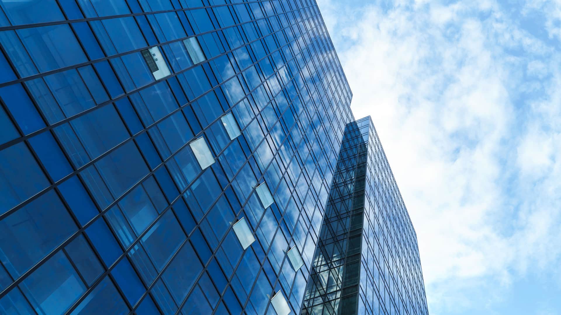Up close to a tall sky scraper with blue windows reflecting clouds.
