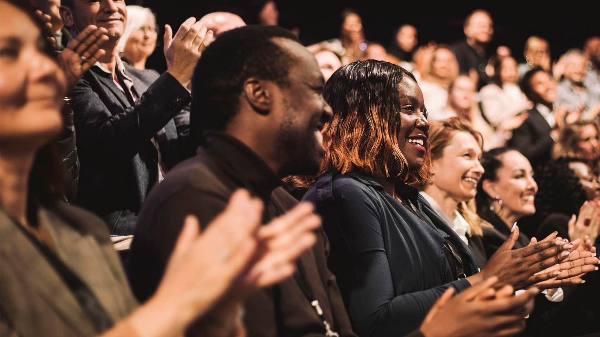 A large group of people who are smiling and applauding during a conference event at a convention center