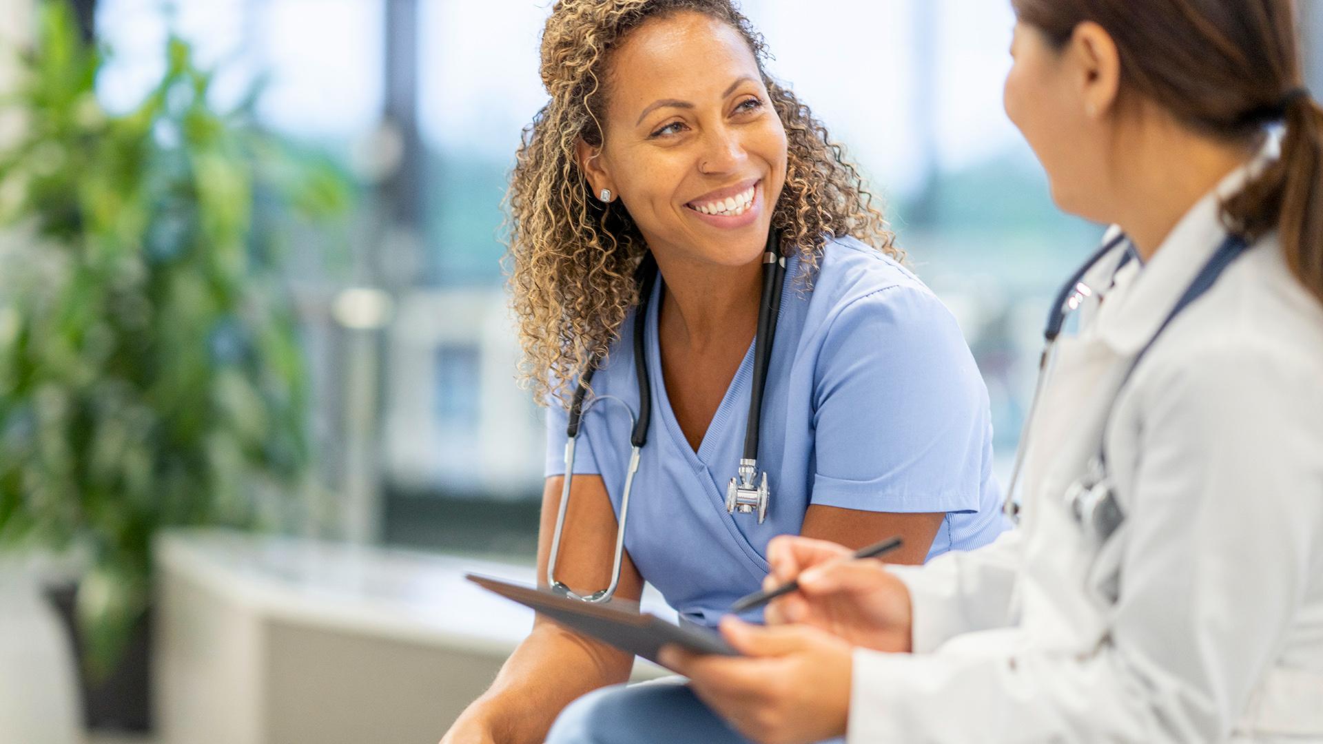 Two female healthcare physicians chatting in a lobby.