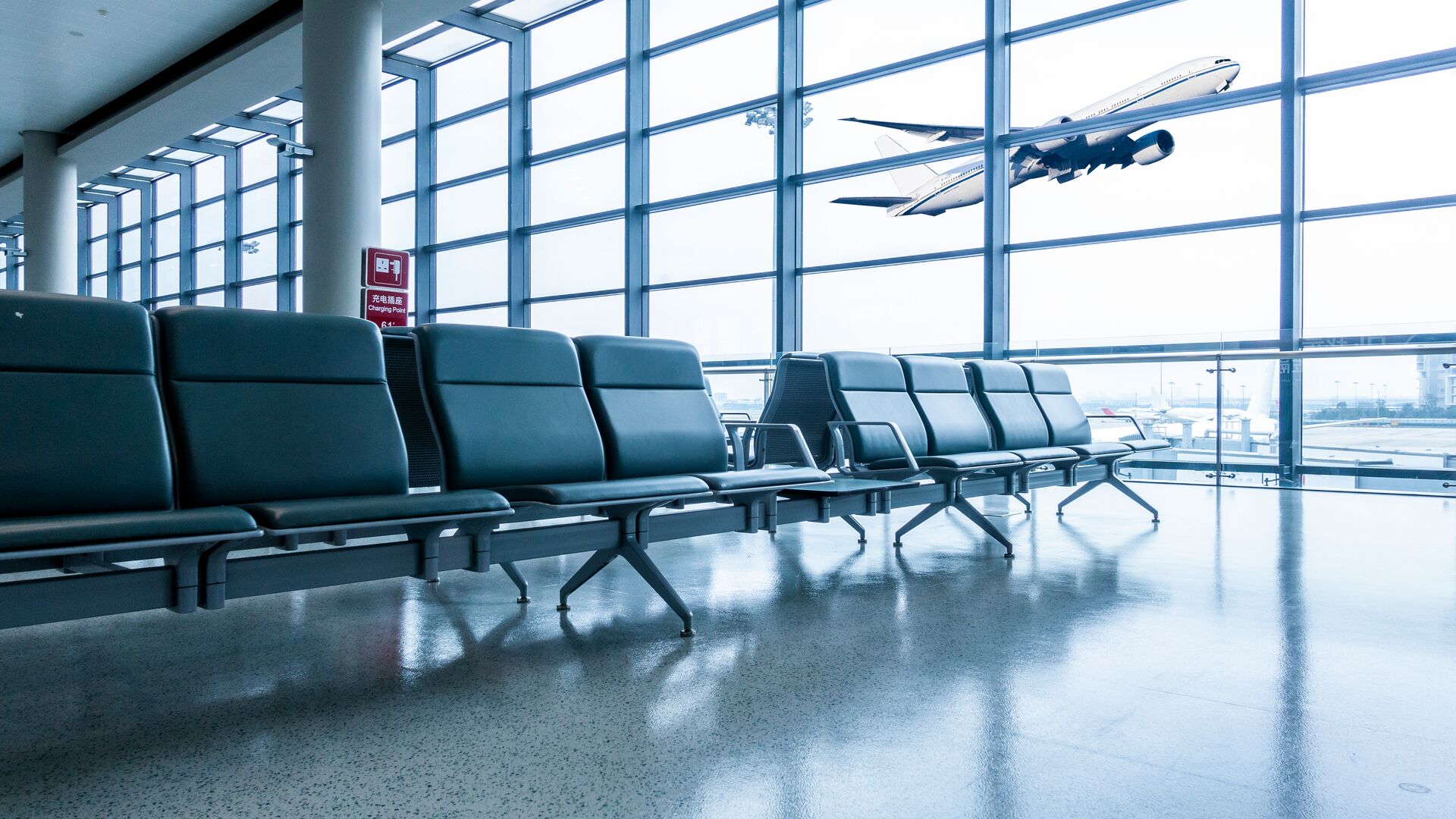 Empty airport terminal seating area with an airplane visible through large windows.