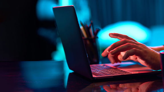 Close up of a person typing on a glowing laptop at night.