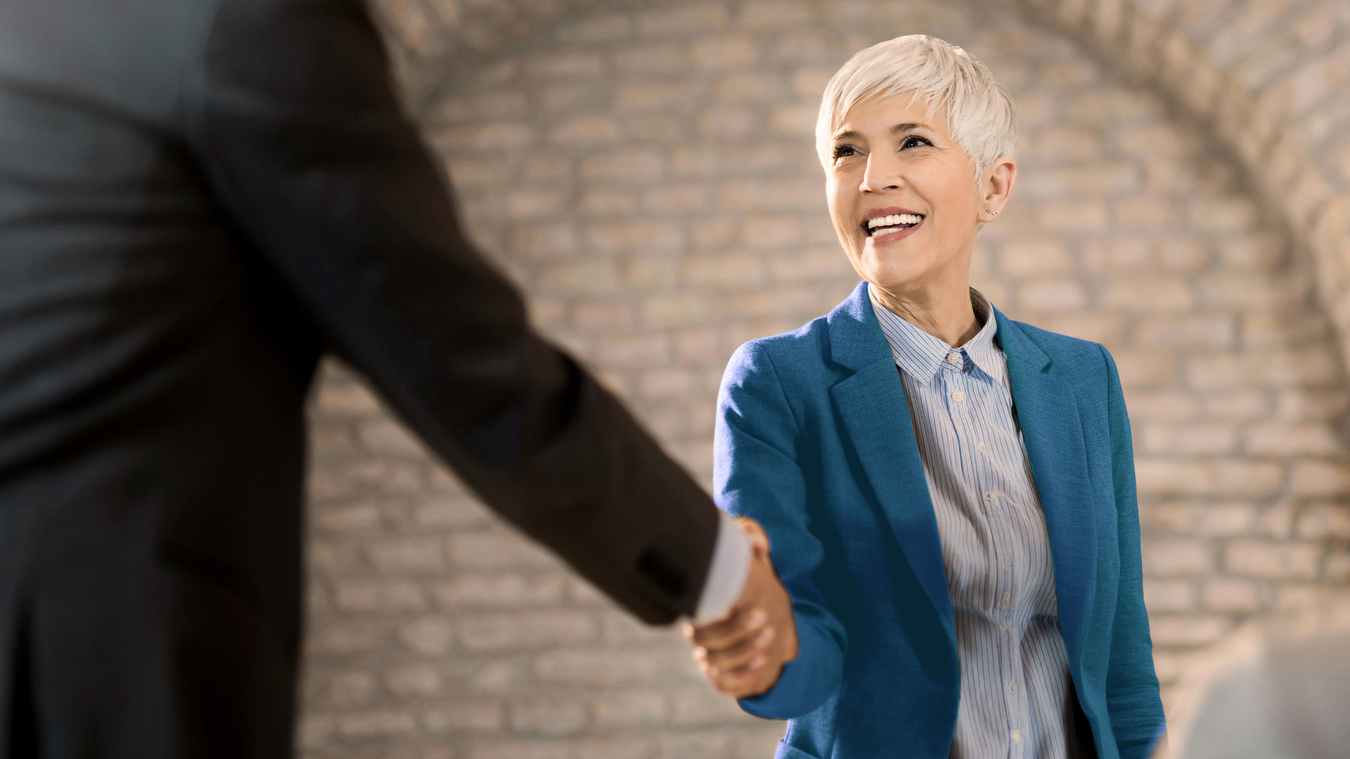 A professional woman shaking hands with a buisnessman.