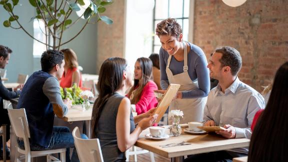 A restaurant server taking an order from a young couple in a hip restaurant.