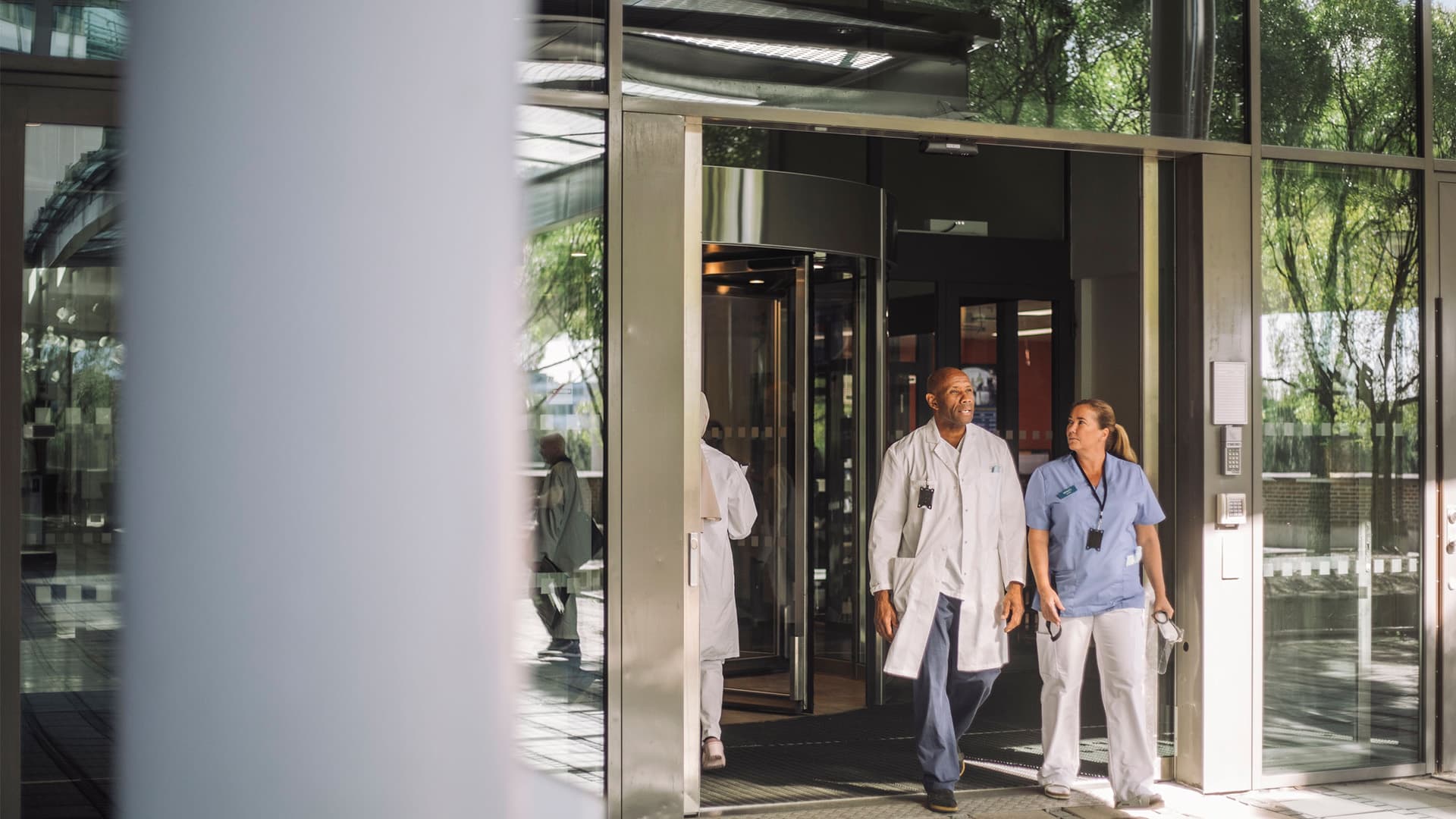 A male and female medical professionals walking out of a hospital building