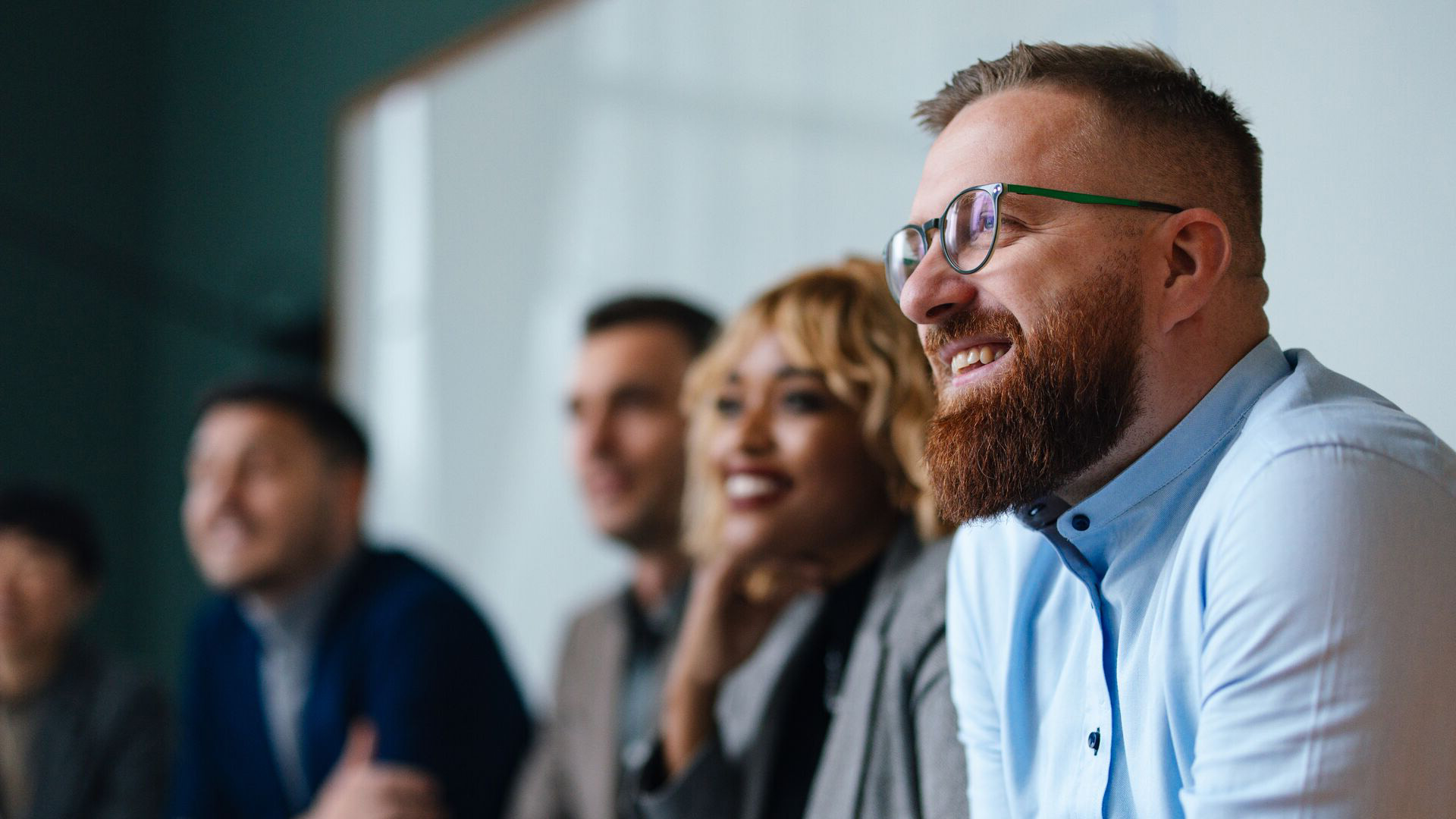 A smiling man sitting next to his colleagues while in a meeting.