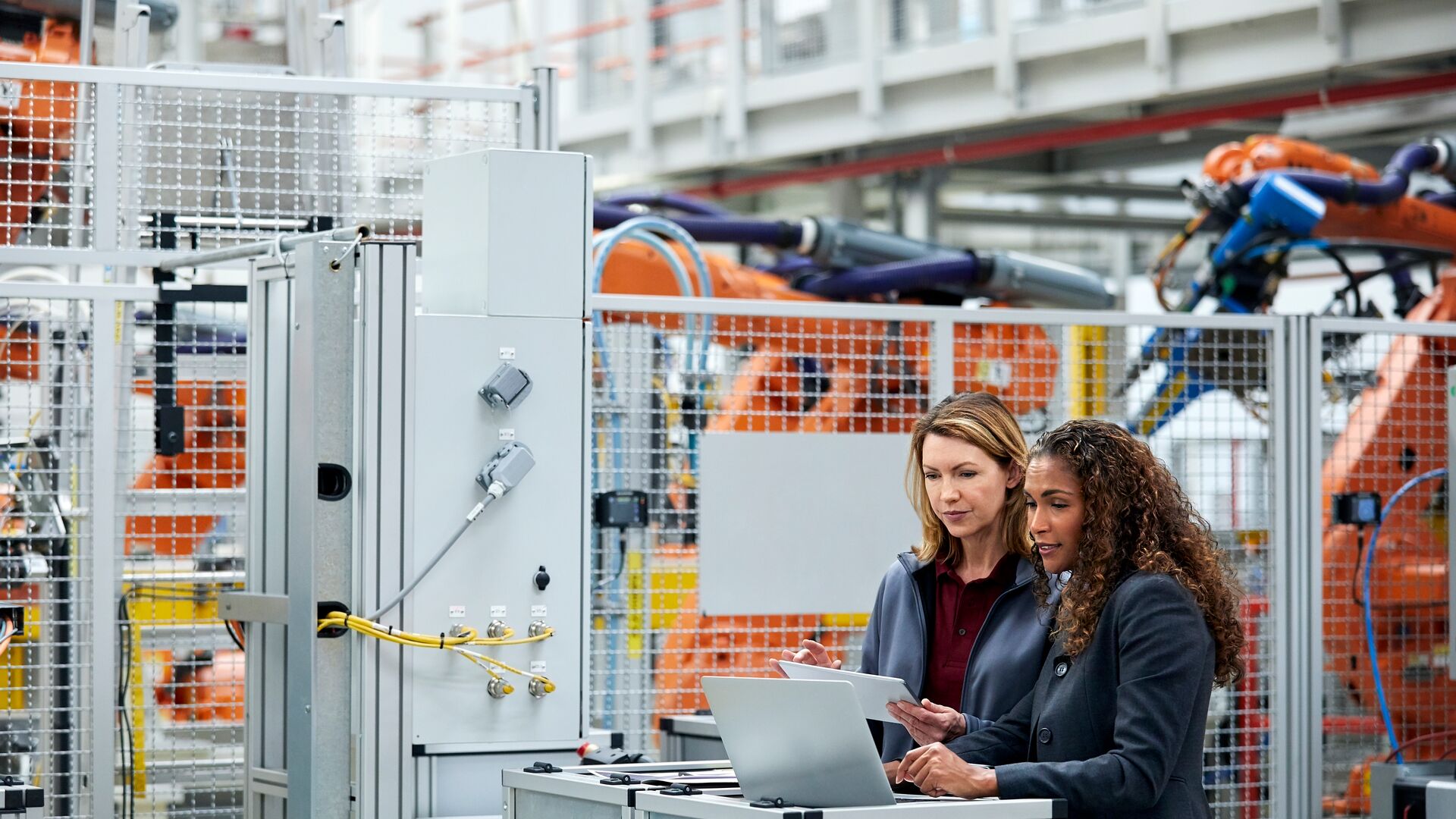 Two female colleagues discussing while standing in car plant.