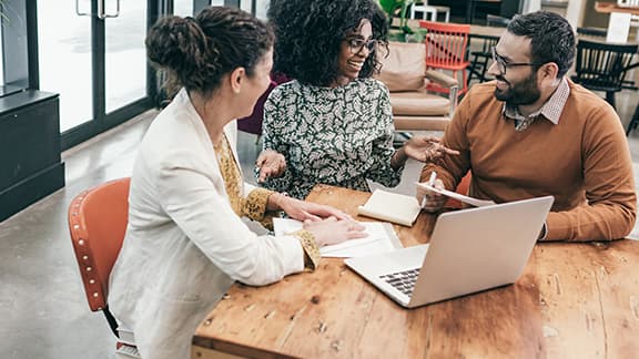 Three people in discussion with a laptop and papers.