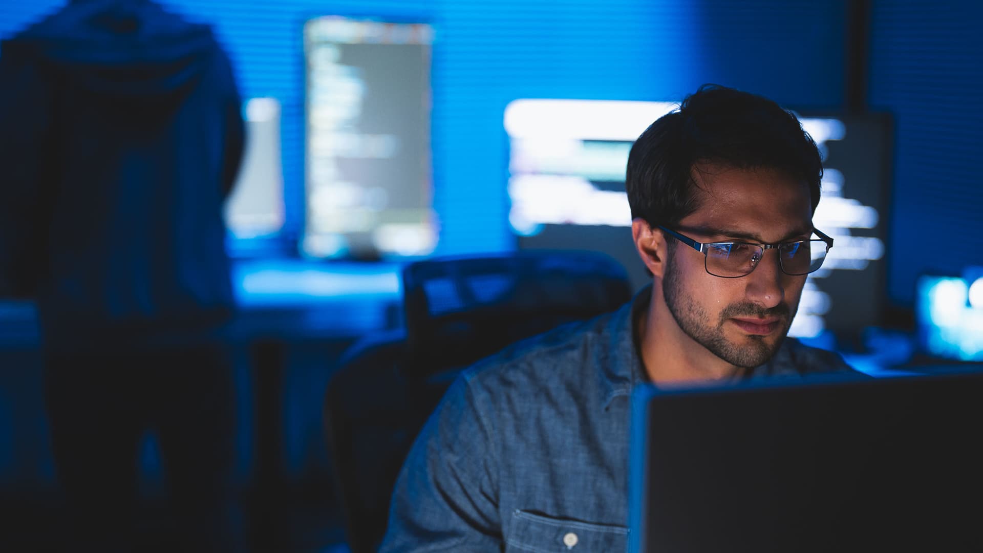 A person sitting and looking at a computer screen while surrounded by other computer screens