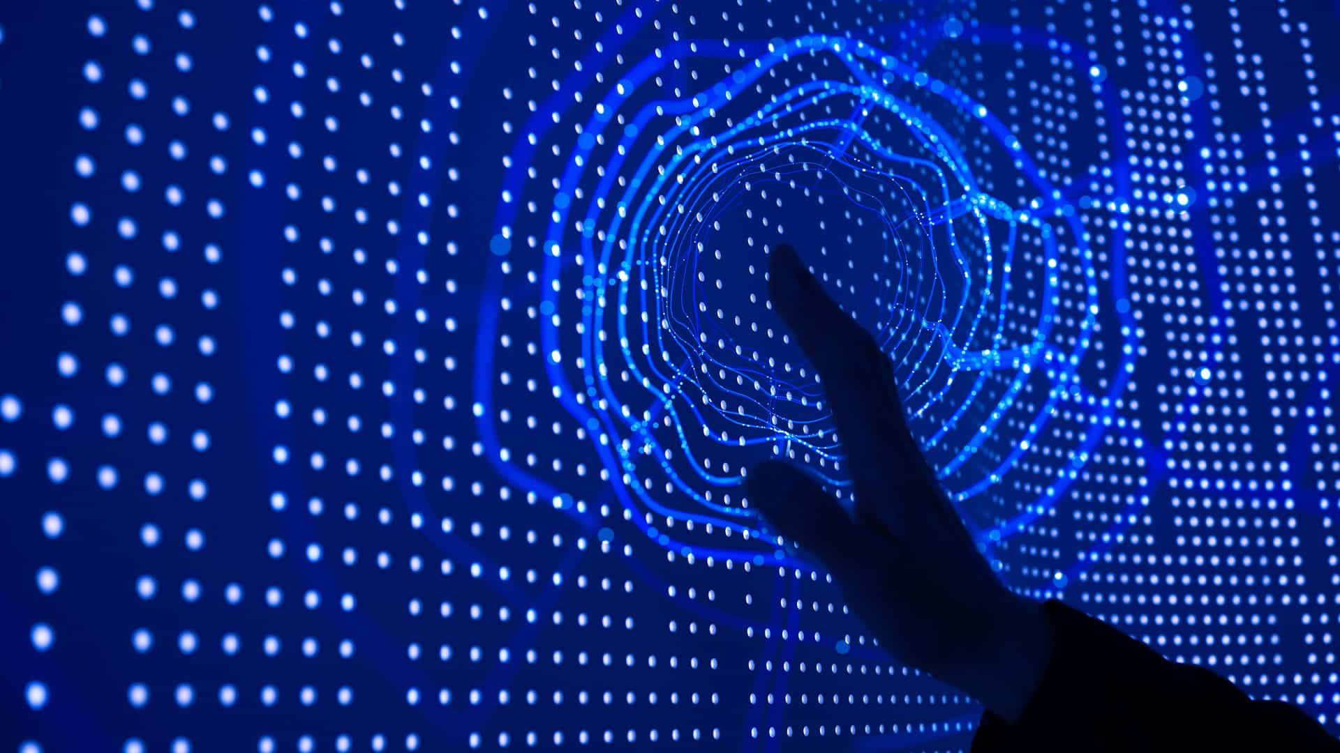 A person touching a screen with their left hand with blue dots and circles displaying on the screen