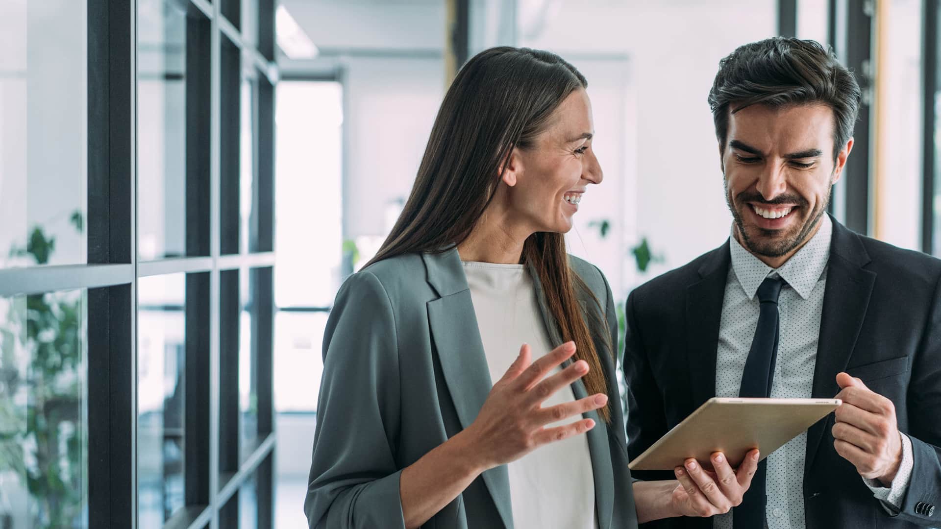 A man and a woman colleague smile while looking at information on a tablet.