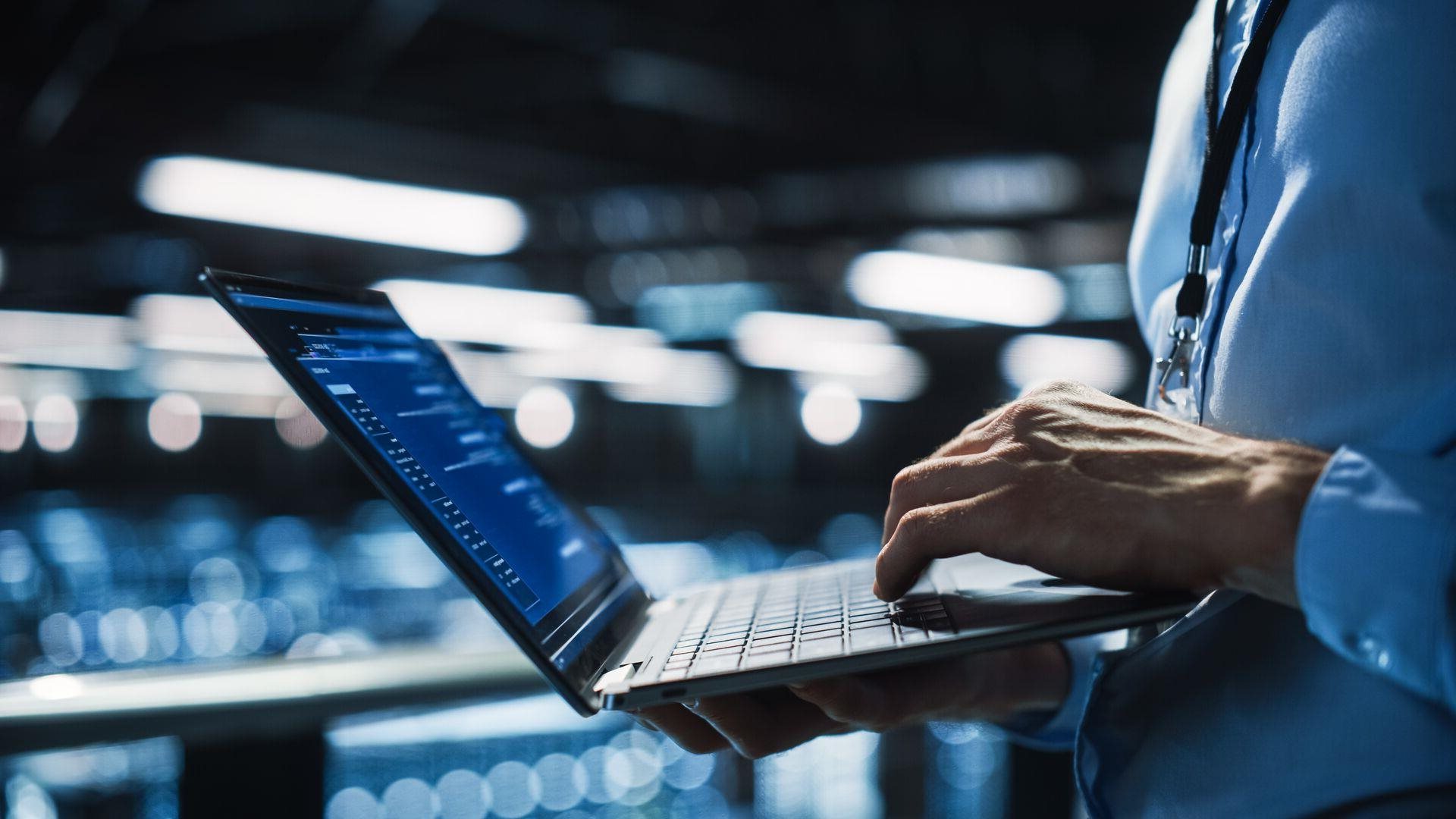 Close up of a person holding a laptop while scrolling in an office.