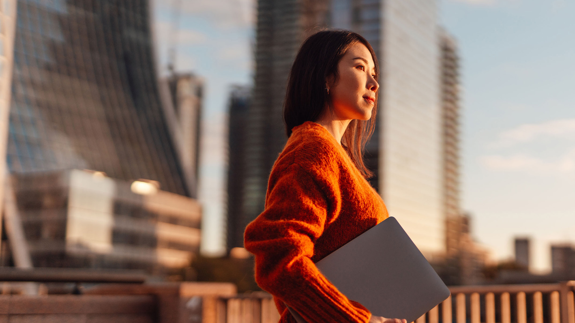 A woman carrying her laptop while walking in a big city.