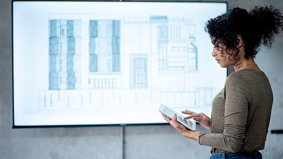 A women who is looking at a digital tablet and going over blueprints and designs