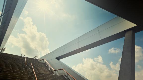 A stairway that is leading up to a blue sky with the sun over light clouds 