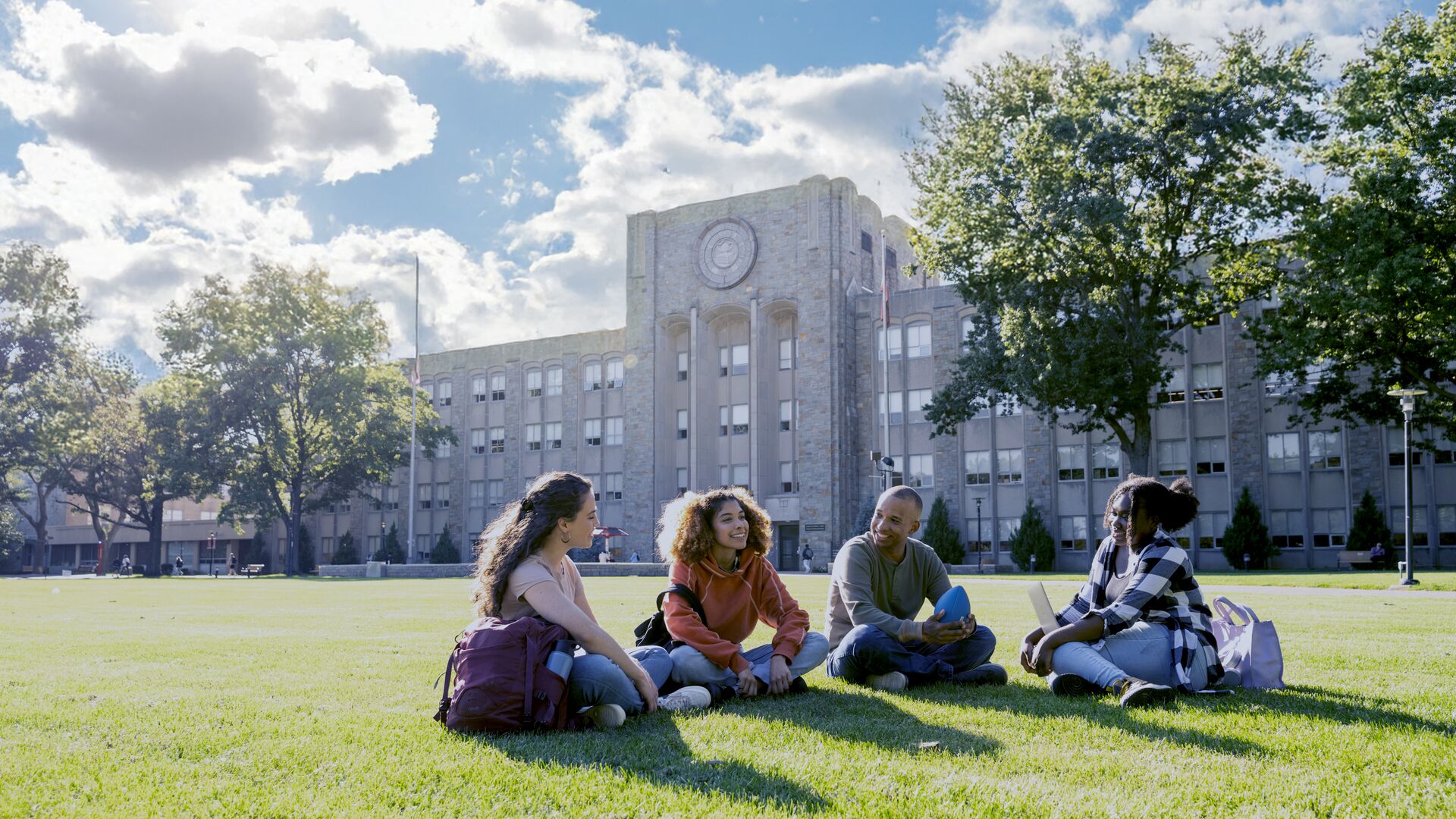 Four college students sitting on green grass near their college campus.