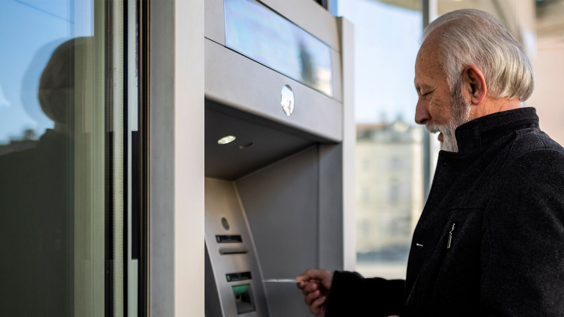 An older man who is using his credit card at an atm.