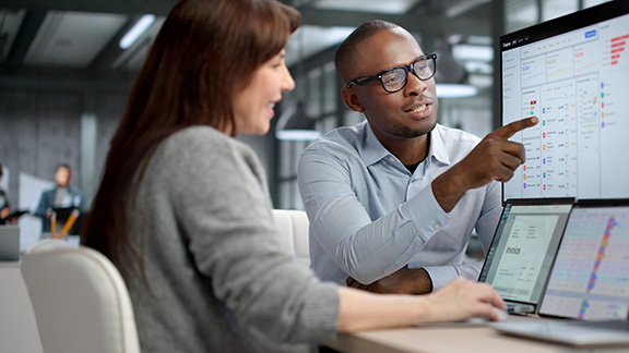 Two professionals analyze financial reports and track data on computer screens.