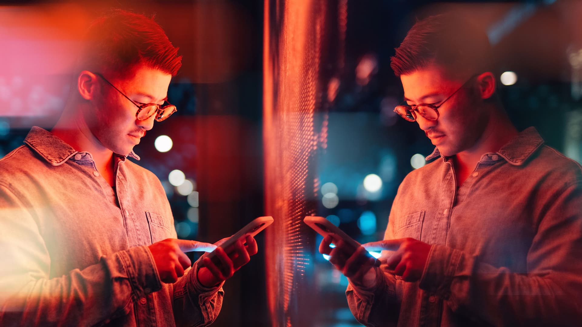 A person using their smartphone next to a futuristic digital display at nighttime