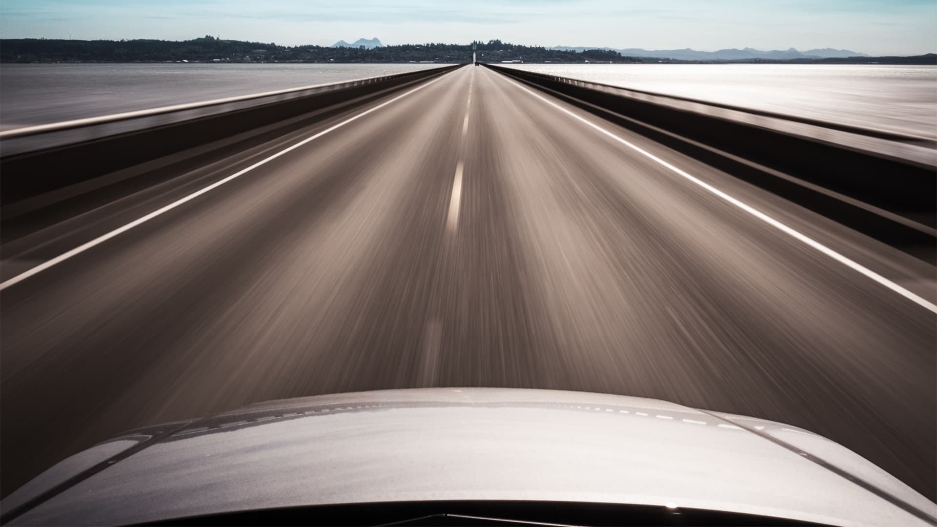 Blurred image of a road and landscape from the hood of a white car.