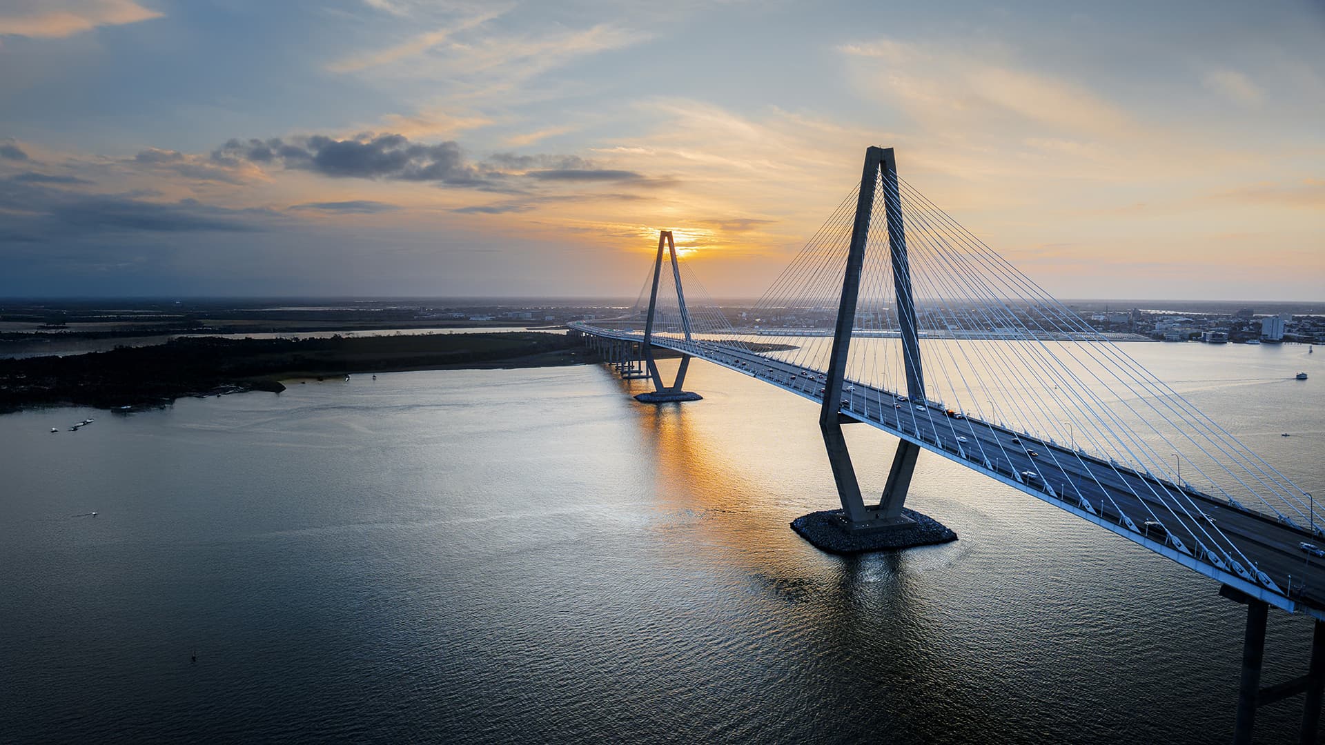 An aerial view of the Arthur Ravenel Jr. Bridge in Charleston, South Carolina, glowing under the vibrant hues of sunset.