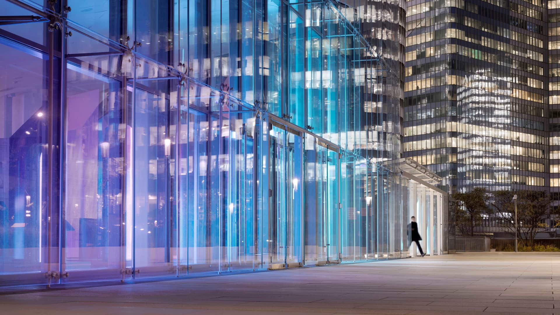 A person walking out of a modern high rise building at night.