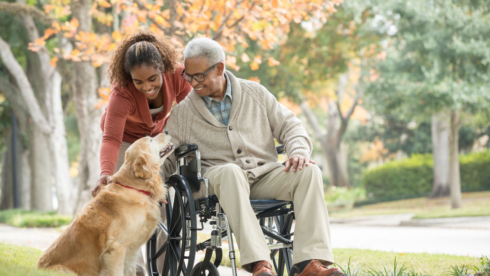 A father and daughter on a sidewalk petting a golden retriever