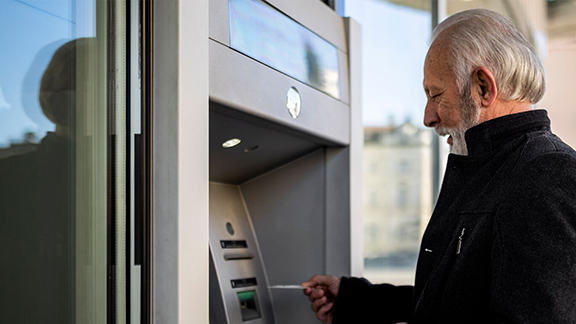 An older man who is using his credit card at an atm.