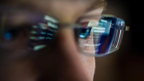 A programmer working on a computer while the screen reflects on his glasses