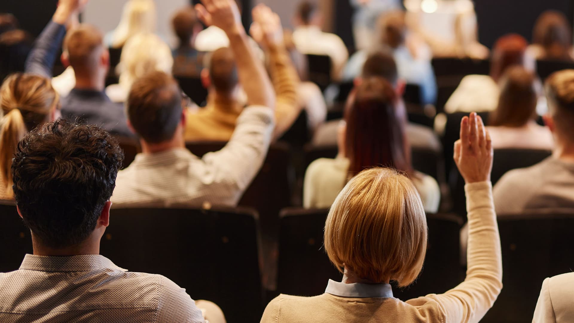 The back view of a crowd of people raising their hands during a seminar at a convention center