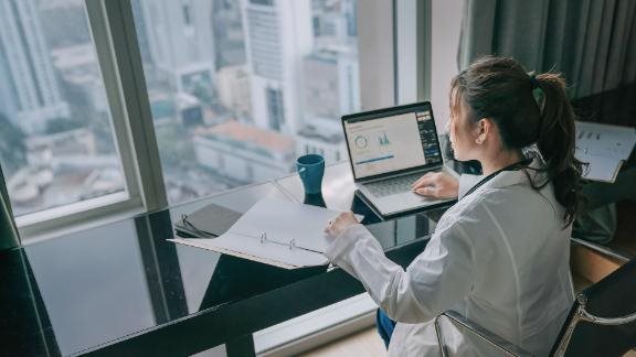 Asian chinese female doctor working on medical report with laptop and document file 