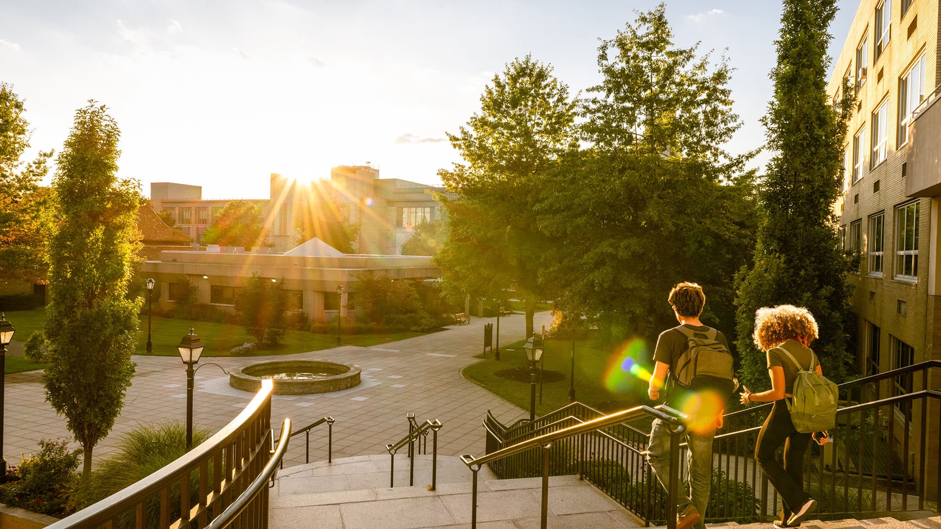 Rear view of two university students walk down campus stairs at sunset
