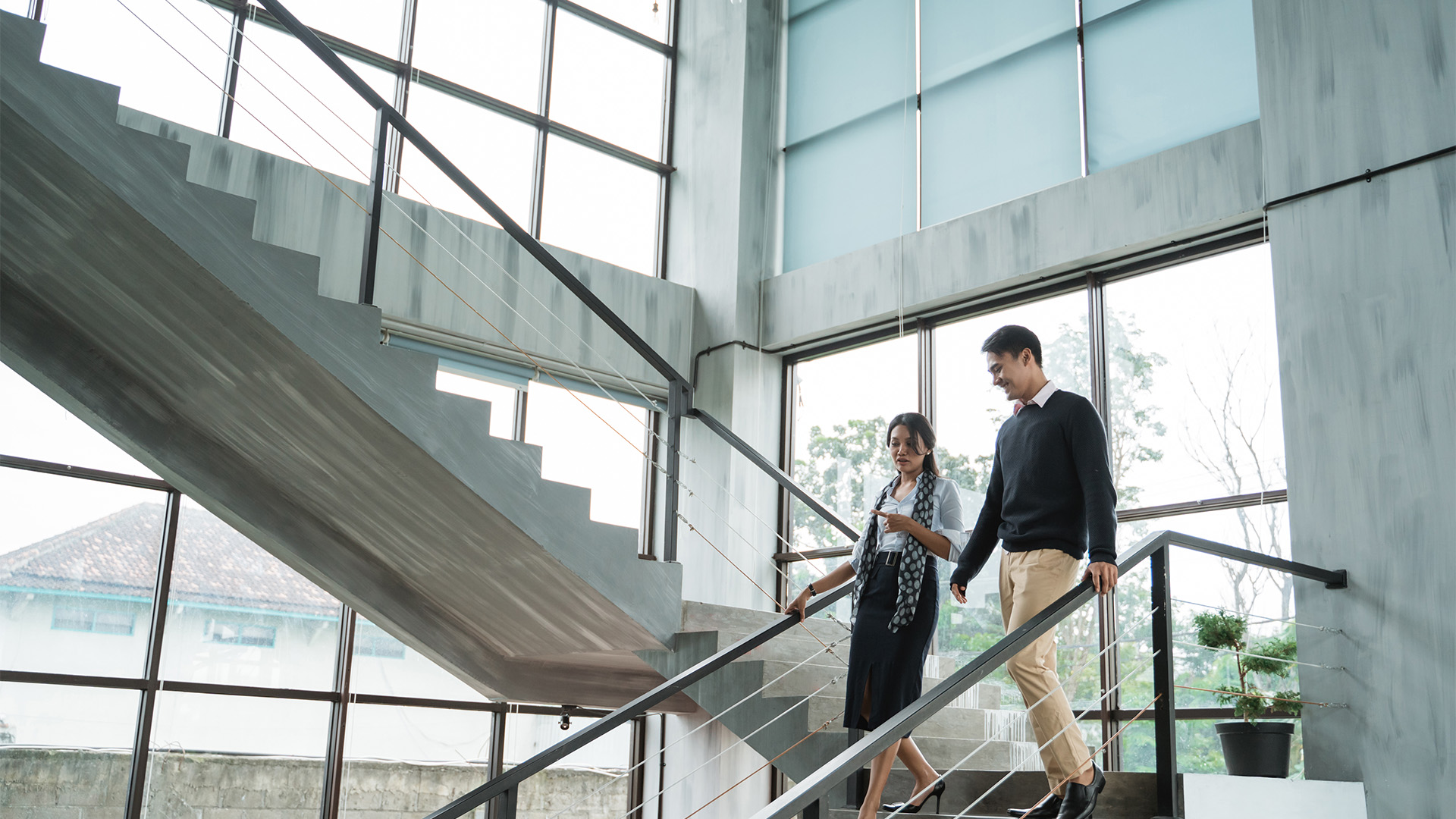 Two people walking down an office staircase and talking with each other.