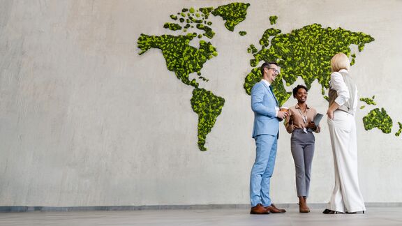 Three people standing in front of a wall that has a map of the world on it.