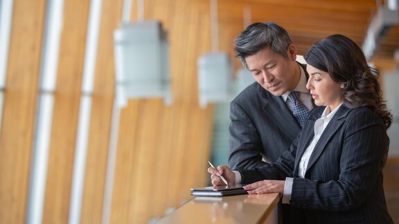 A man and women standing on an office balcony and taking notes
