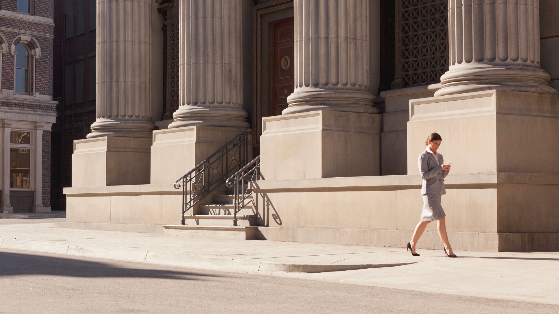 A professional woman walking outside of a government building looking at something on her phone.