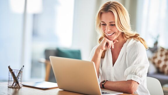 A smiling women sitting at a desk while working on a laptop