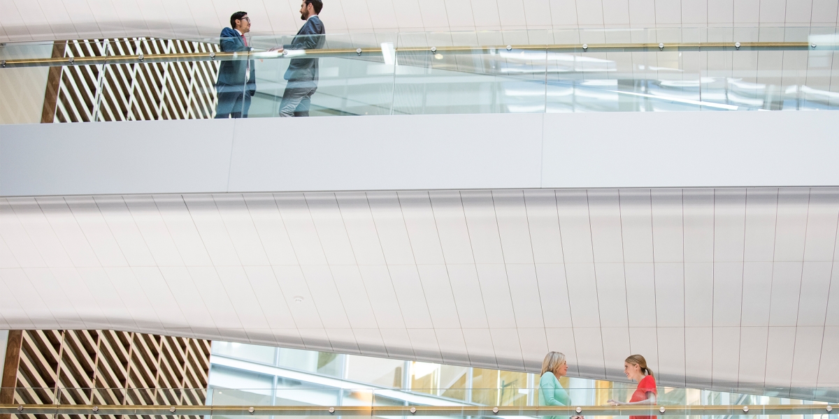 Two coworkers conversing on glass walkway.