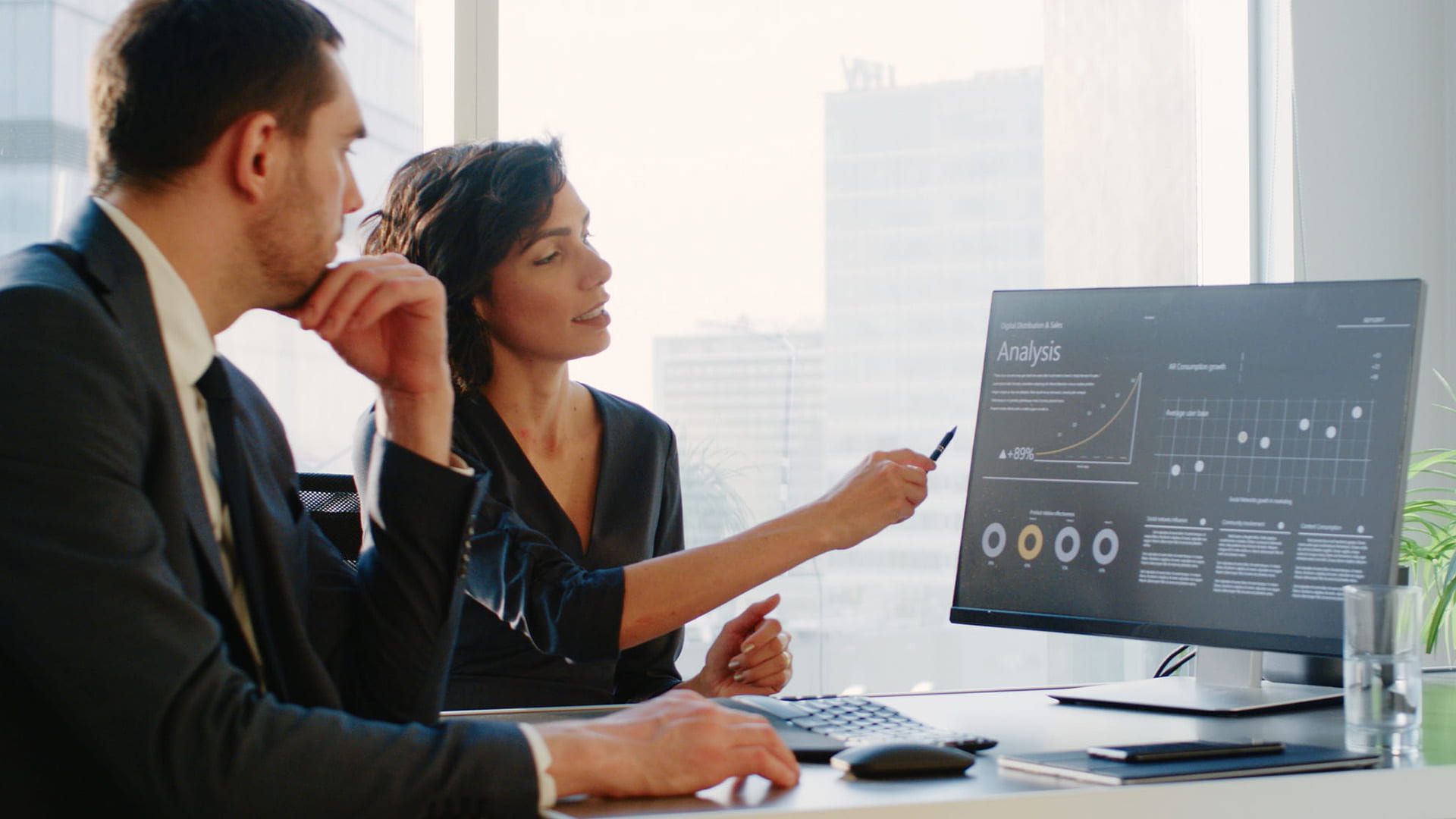 Two professionals looking at data on a computer in a skyrise office.