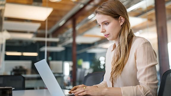 A woman reading on her laptop at her desk in an office.