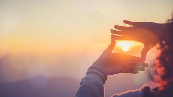A person framing the sun with her hands at sunset.