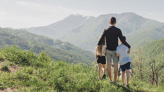 A Dad and his children standing on top of a large hill looking at the mountains in the distance