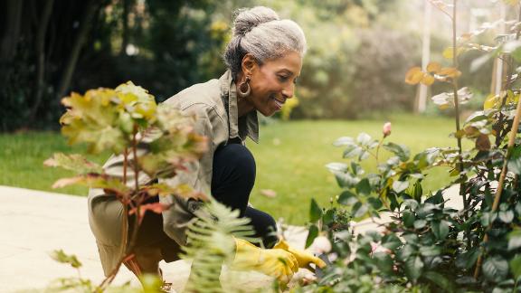 Side view of smiling senior woman crouching by plants.
