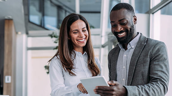 Two people who are smiling and looking down at a digital tablet together