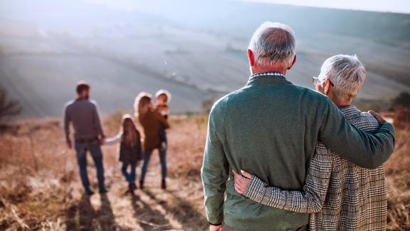Back view of embraced grandparents enjoying while looking at their family on a field in autumn day.