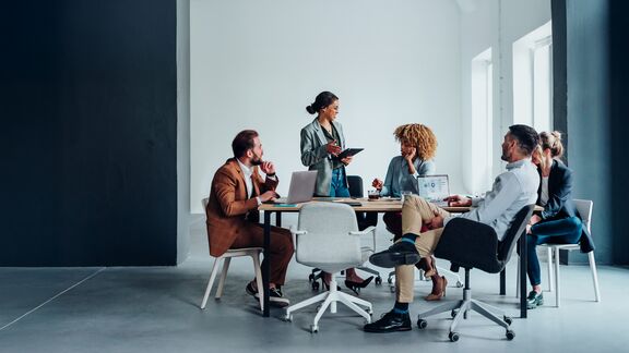 A group of people who are sitting at a table with laptops and having a discussion