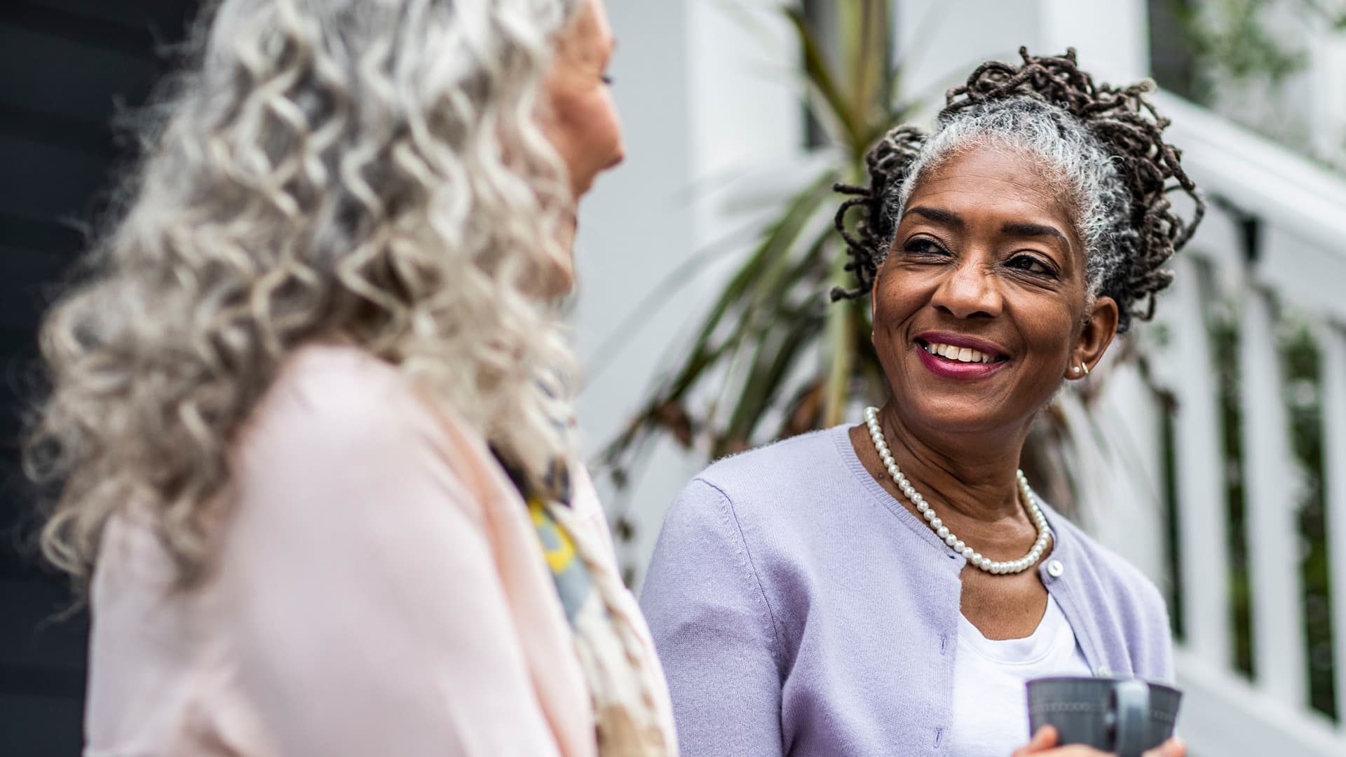 Older women talking and having coffee on the front steps of a home