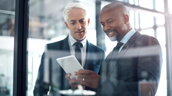 Two smiling colleagues using a digital tablet together in an office.