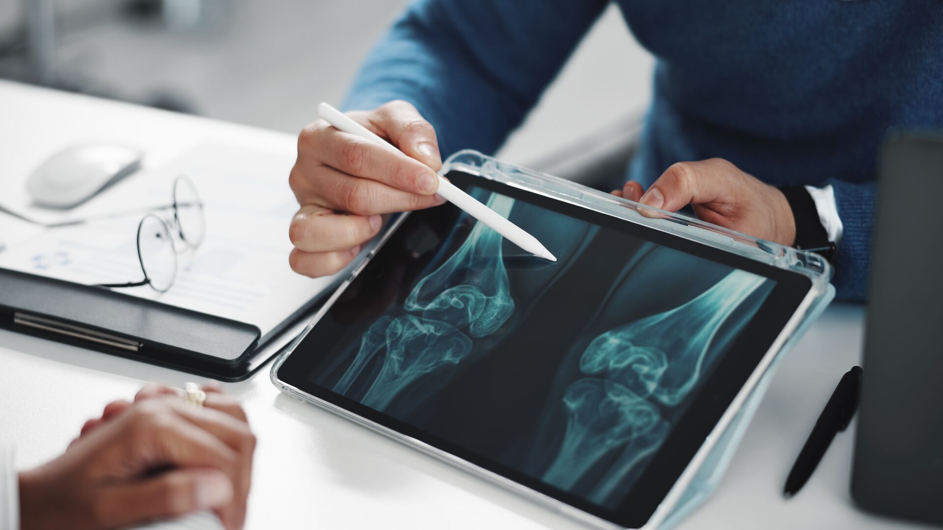 A doctor and a patient going over a knee x-ray on a digital tablet.
